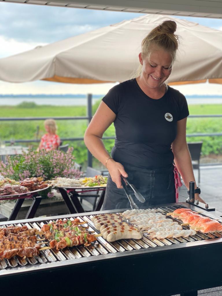 Medewerkster bakt spiesjes, worst, garnalen en zalm op de barbecue op het terras