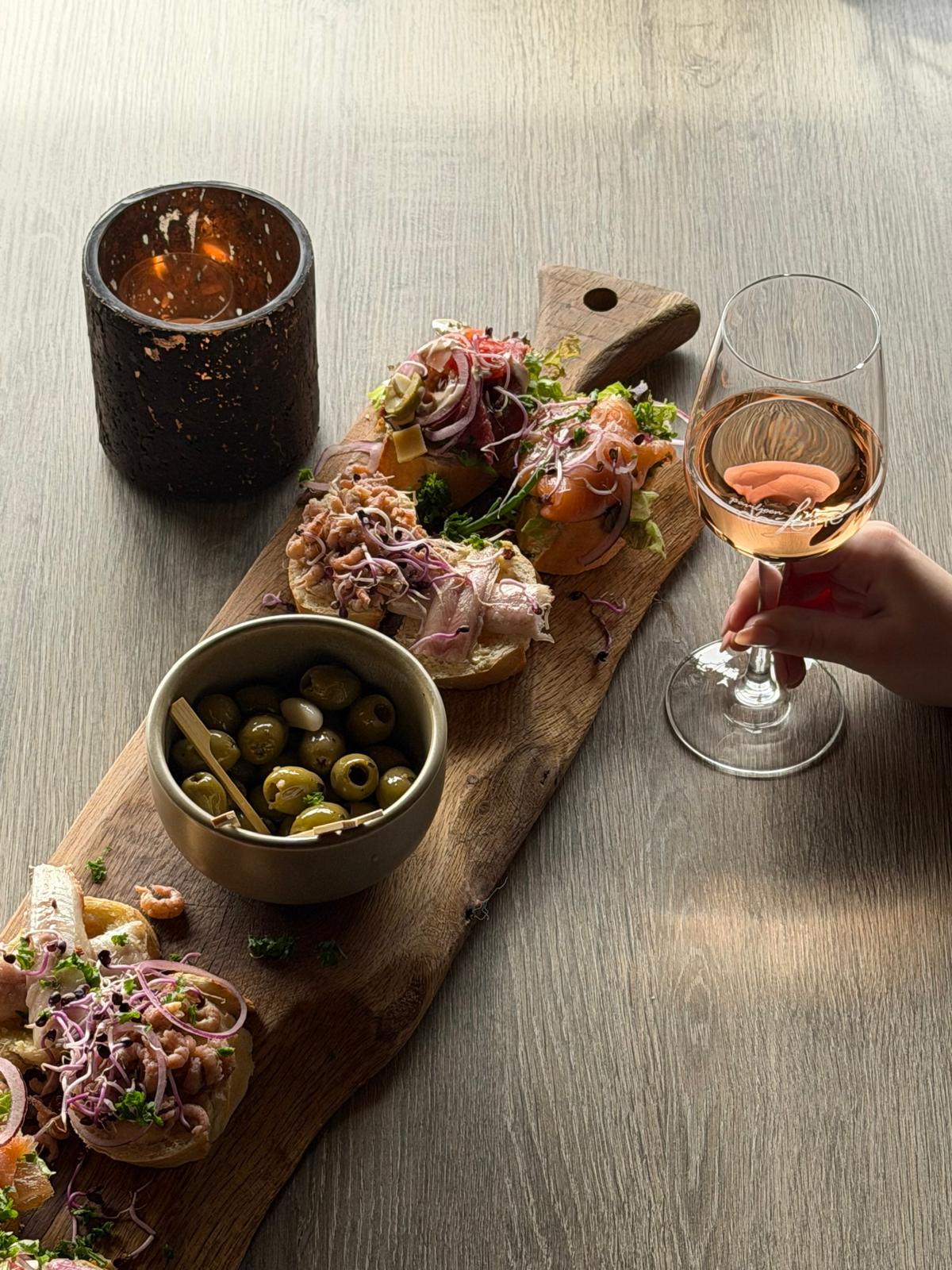 Borrelplank met belegde broodjes, olijven en een glas rosé